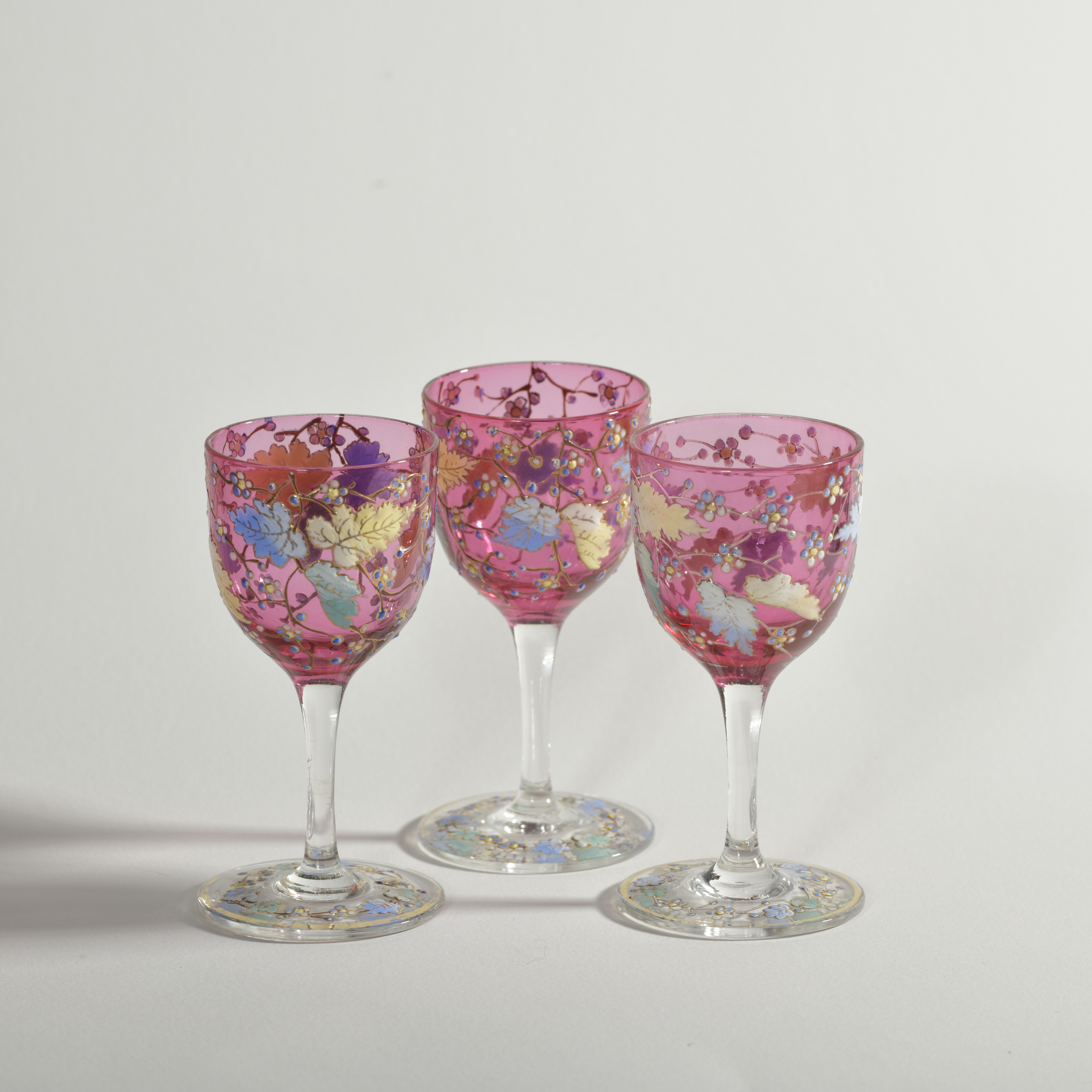 Three Antique Moser style ruby sherry or port glasses with enamelled leaves, vines and flowers